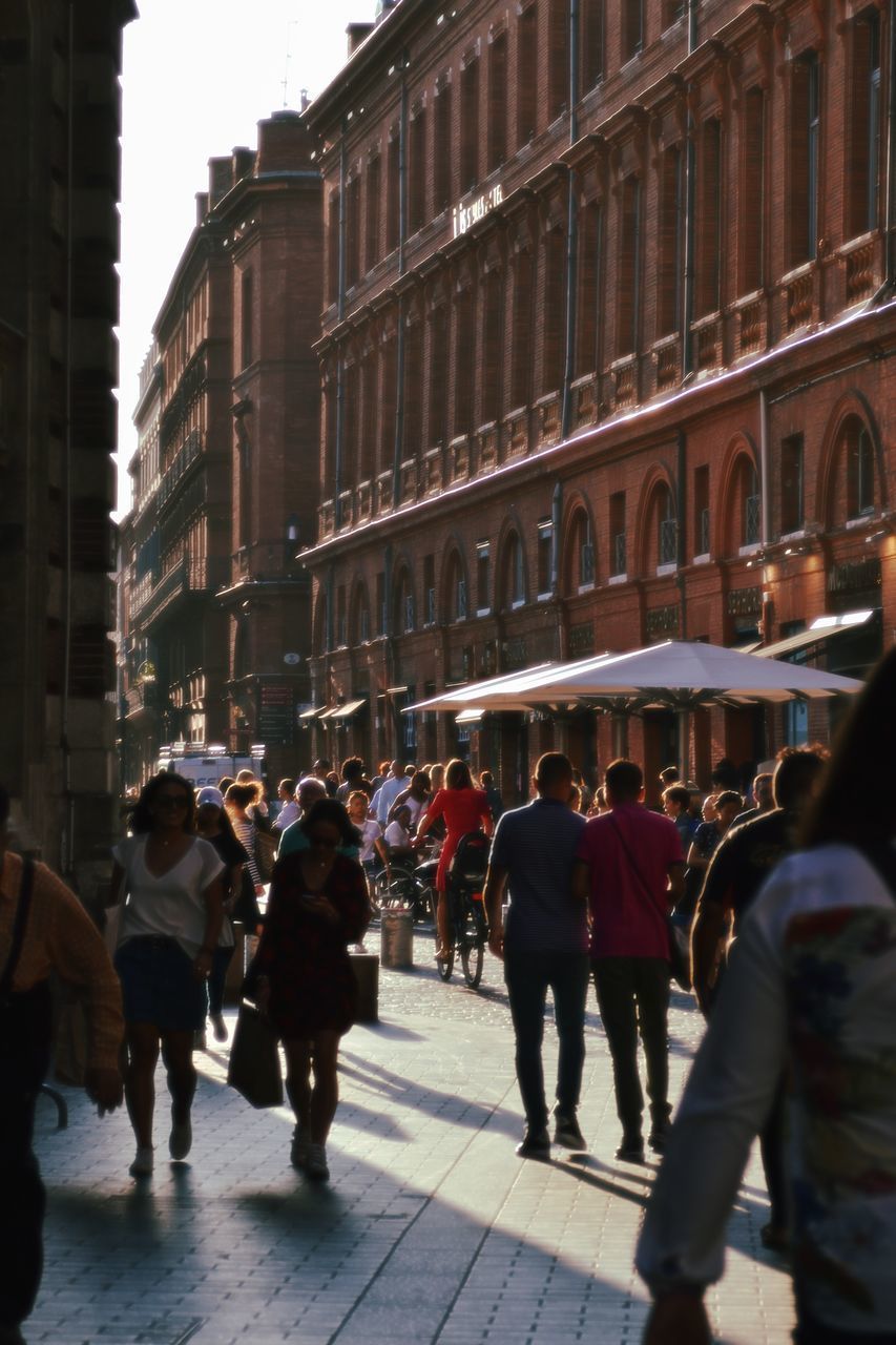 PEOPLE WALKING ON STREET AMIDST BUILDINGS