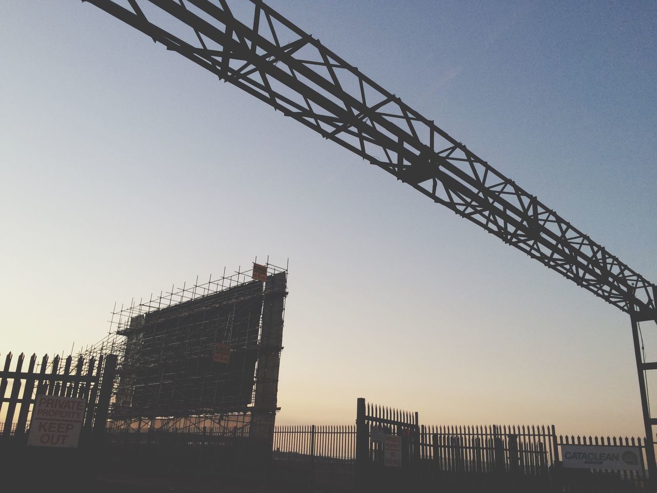 clear sky, built structure, architecture, low angle view, construction site, copy space, building exterior, silhouette, metal, crane - construction machinery, construction, development, sky, metallic, industry, incomplete, outdoors, crane, connection, sunset