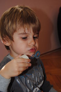 Close-up of cute boy blowing bubble while sitting at home