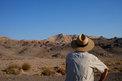 Rear view of woman standing at desert against clear blue sky