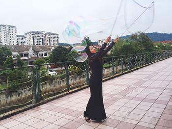 Portrait of woman standing by tree against sky in city