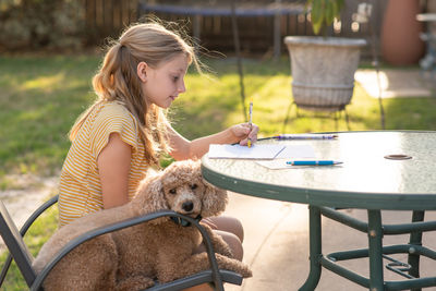 Girl writing on paper sitting with her pet dog