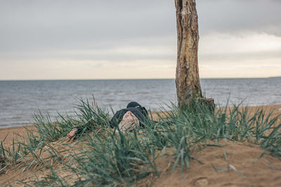 Young woman exercising while lying down by tree trunk at beach