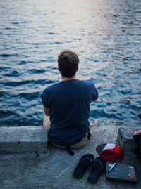 Rear view of man sitting on pier against sea