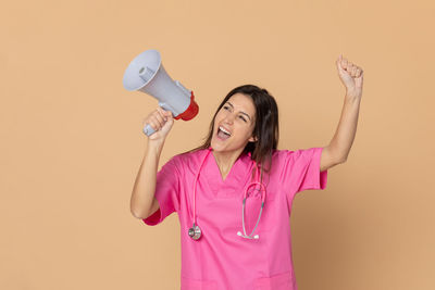 Woman with arms raised standing against pink background