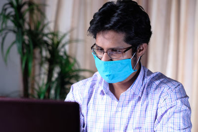 Close-up of doctor wearing mask using laptop at office