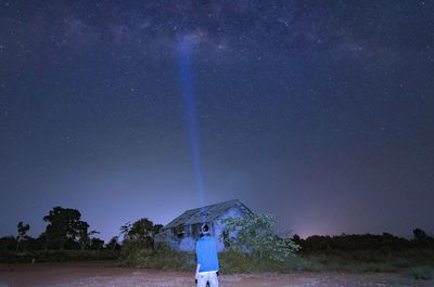 Rear view of man with flashlight standing on field against sky at night