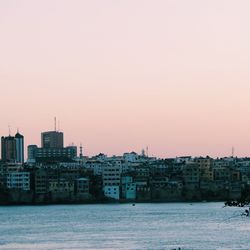 Buildings in front of river against clear sky at dusk