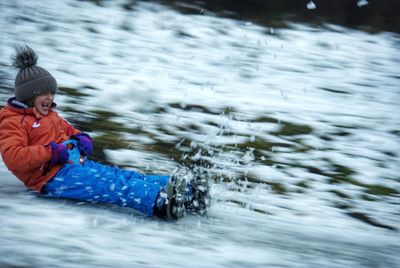 Blurred motion of girl sitting on sled while sliding on snow