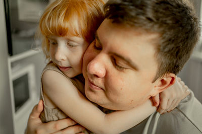 Man with eyes closed hugging daughter at home