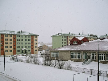 Houses by snow covered buildings against clear sky