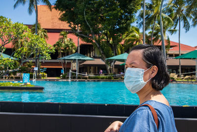 Woman wearing mask looking away while standing by swimming pool