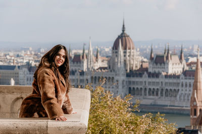 Portrait of beautiful young woman on balcony overlooking hungarian parliament in budapest, hungary