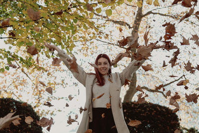 Portrait of smiling young woman standing by cherry blossom tree