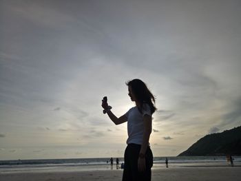 Side view of woman standing at beach against sky during sunset