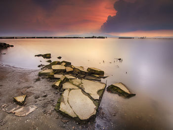 Scenic view of rocks by sea against sky during sunset