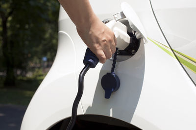 Cropped hand of woman charging electric car at station