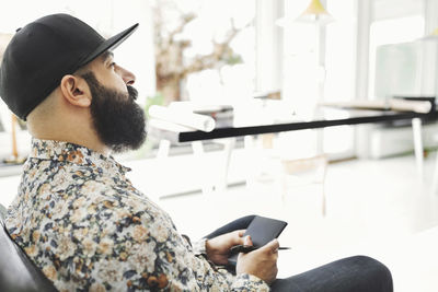 Side view of male architect holding note pad while sitting in home office