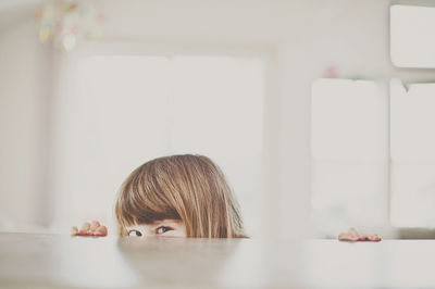 Portrait of girl peeking over table at home