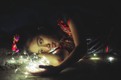 Portrait of cute girl lying on illuminated mirror
