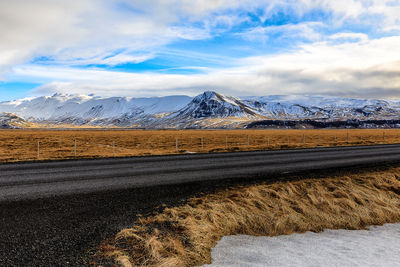 Road amidst field against snowcapped mountains