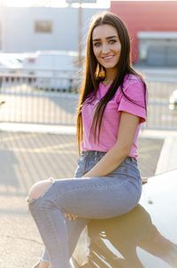 Portrait of smiling young woman sitting on seat in city