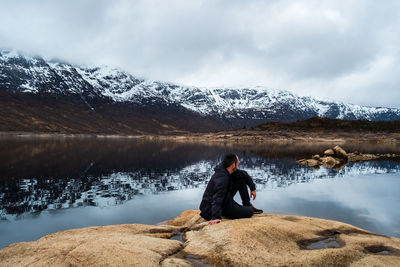 Woman on snowcapped mountain by lake against sky