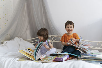 Two kids reading piles of books in bed and laughing