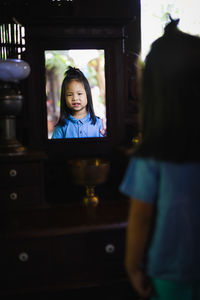 Rear view of cute girl with long hair looking in mirror at home