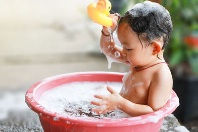 Cheerful shirtless baby girl sitting in bathtub