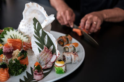 Close-up of sushi served in plate while cropped hands cutting food in background