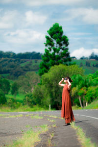 Young woman wearing sunglasses standing on road against trees in forest