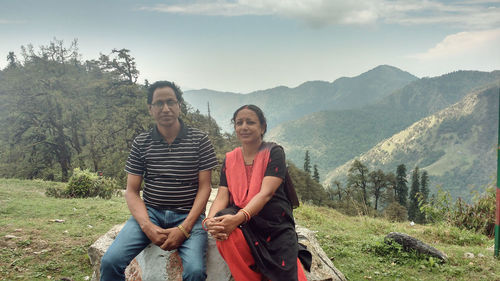 Portrait of mature couple sitting on rock against mountains