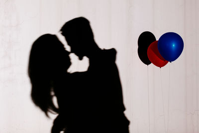 Shadow of couple embracing on wall by balloons