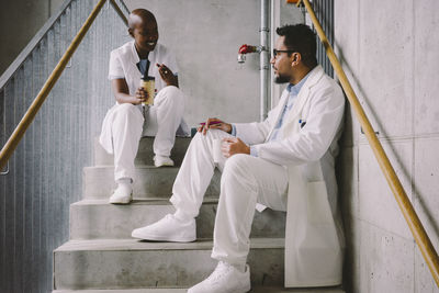 Happy medical colleagues talking while sitting at staircase during coffee break