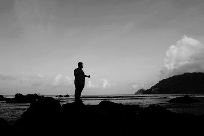 Silhouette man standing at beach against sky