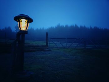 Illuminated farm light on field against foggy sky at night