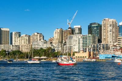 Sailboats in sea by modern buildings against clear blue sky