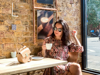 Young millennial woman is drinking morning coffee at a local cafe shop by the window. wearing dress