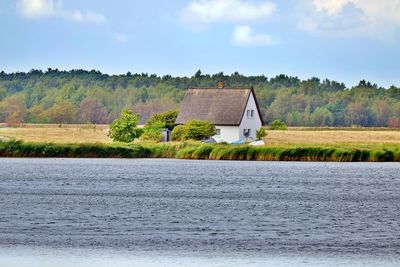 House by lake against sky