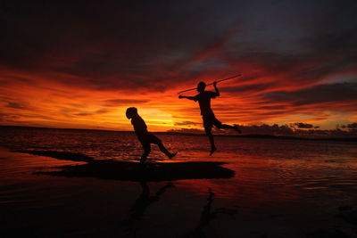 Silhouette men standing on beach against sky during sunset