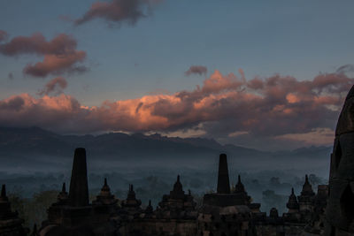 Silhouette temples against cloudy sky during sunset