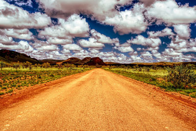 Dirt road amidst field against sky