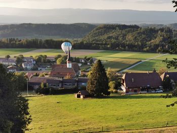 Houses and a hot air balloon on field by trees against sky