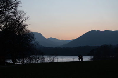 Silhouette trees and couple by lake against sky during sunset