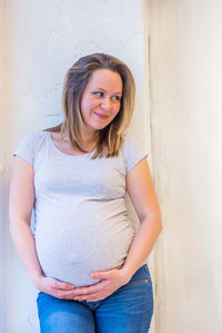 Portrait of smiling young woman standing against wall