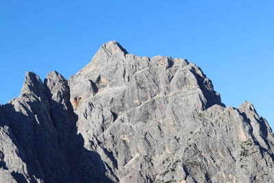 Low angle view of rocky mountains against clear blue sky