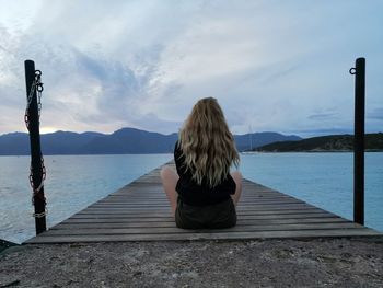 Rear view of woman sitting on pier against sky