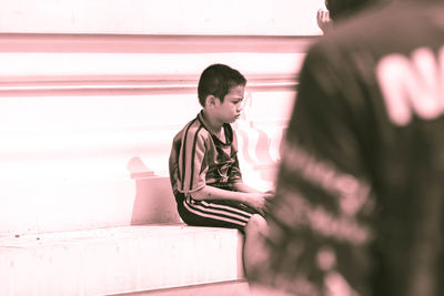 Boy looking away while sitting on wall