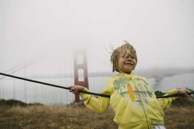 Girl leaning on cable against golden gate bridge during foggy weather